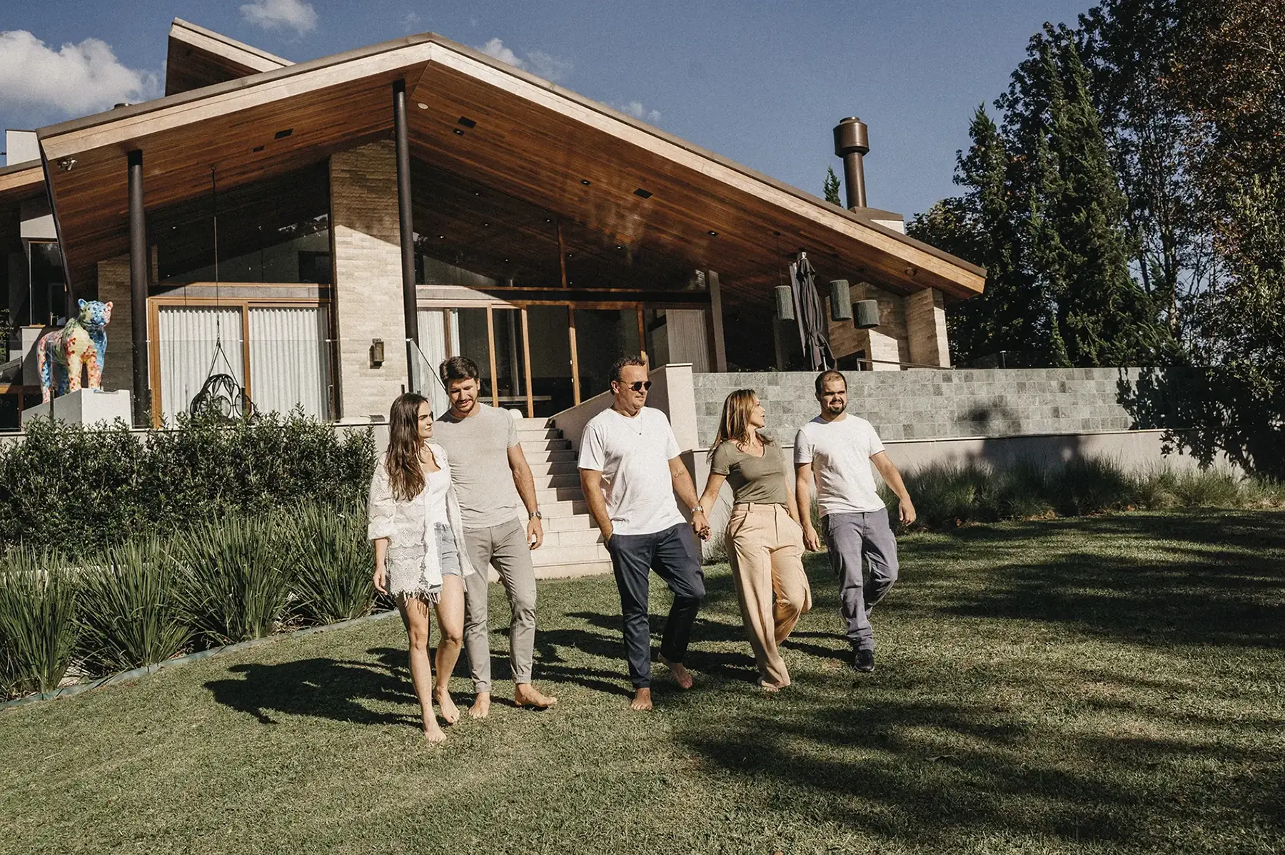 Família caminhando juntos no jardim em frente a uma residência de alto padrão com arquitetura contemporânea, revestimento em madeira e pedra natural