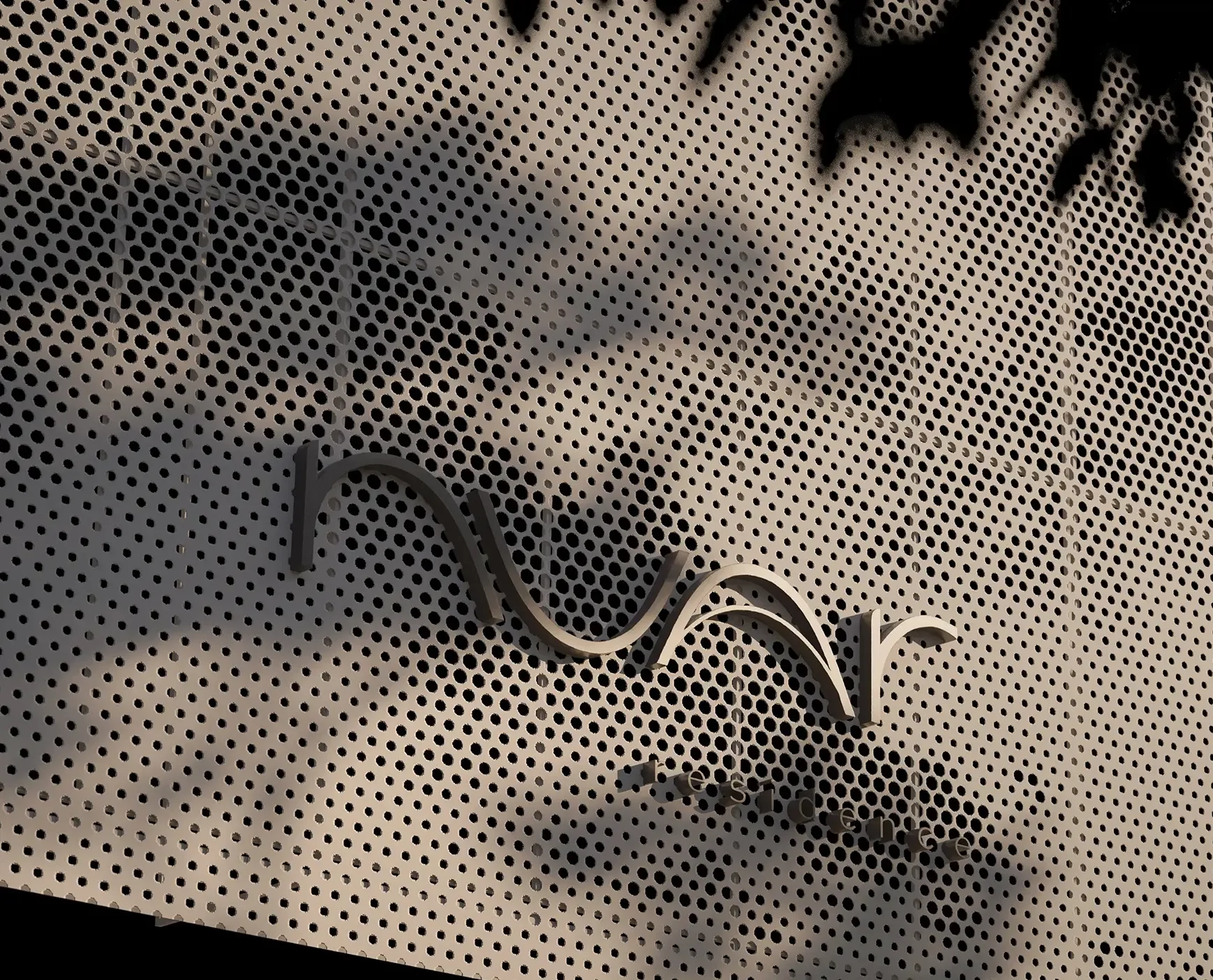 Detalhe da fachada do Nuar Residence em Balneário Piçarras, com logotipo em letras metálicas aplicadas sobre painel perfurado e sombras de vegetação