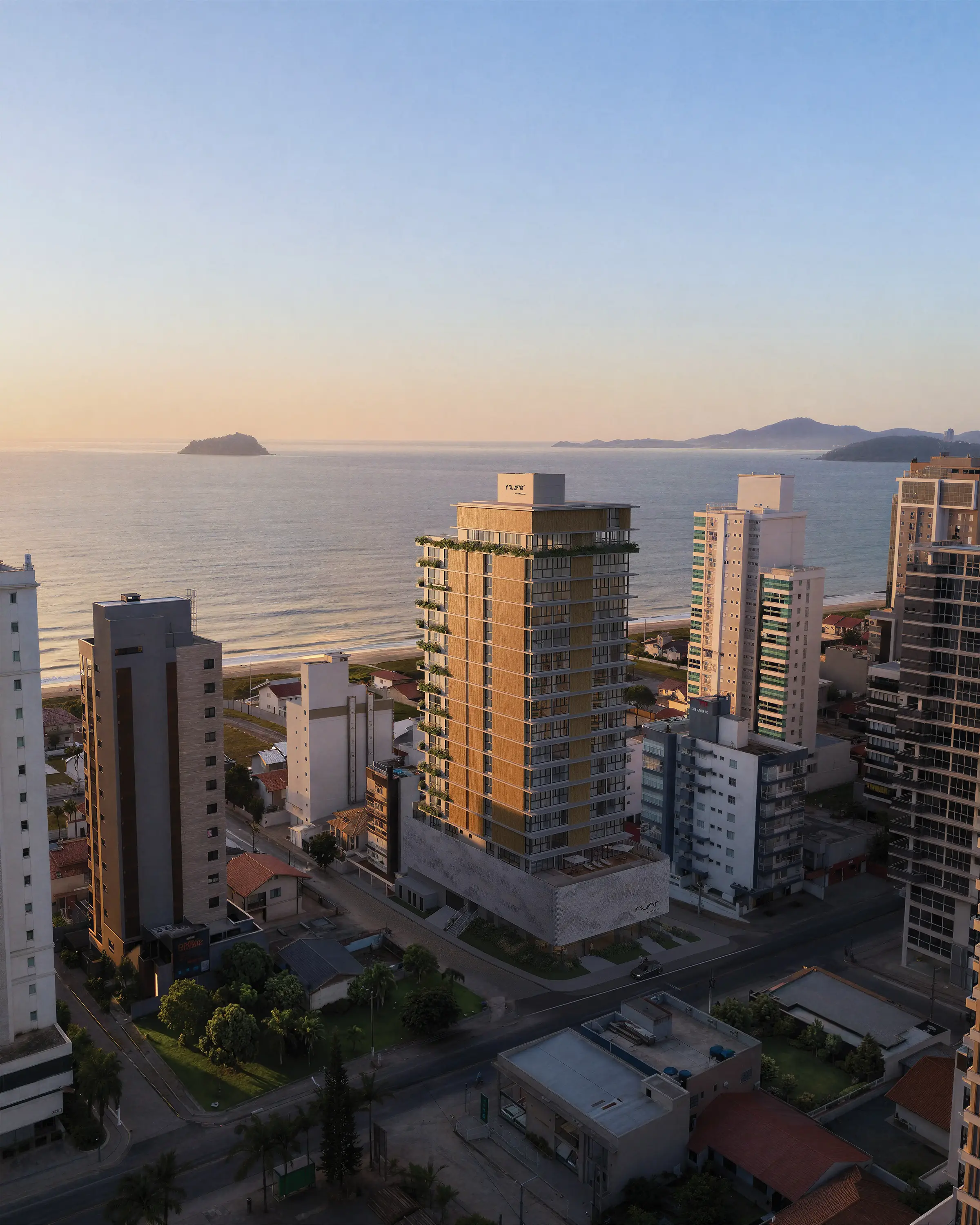 Fotomontagem aérea do Nuar Residence em Balneário Piçarras, inserido no contexto urbano da cidade às margens do mar, com ilhas ao fundo e céu em tons de pôr do sol